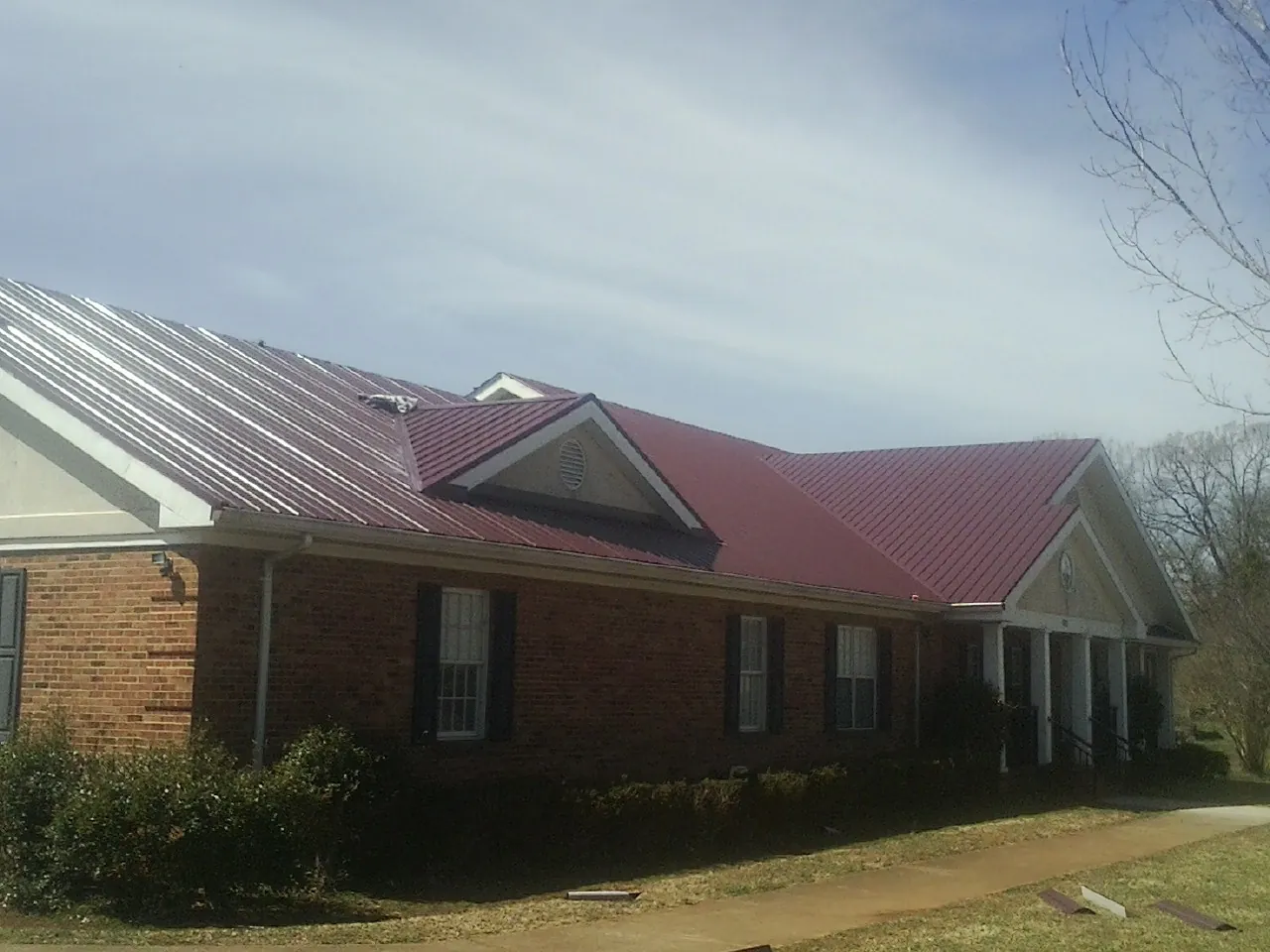 Red metal roof with gabled entries on a long brick building, from a Hail Damage Roof Repair job in Haugan