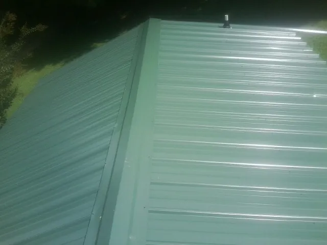 New green metal panels meeting at the ridge of a roof — Flat Roof Repair work by our crew in Haugan