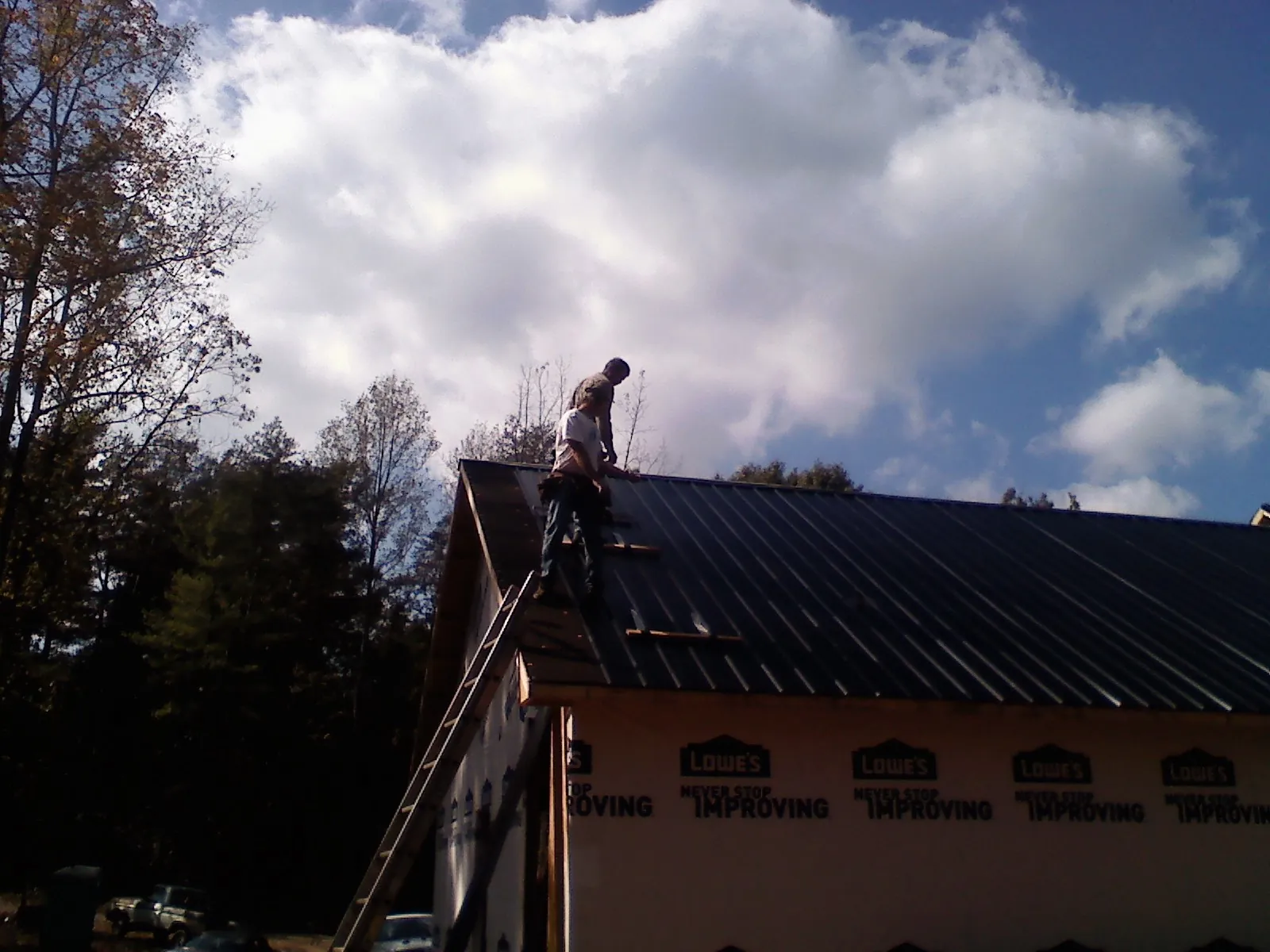 Roofer fastening dark metal panels high against a cloudy sky, from a Roof Inspection job in Haugan