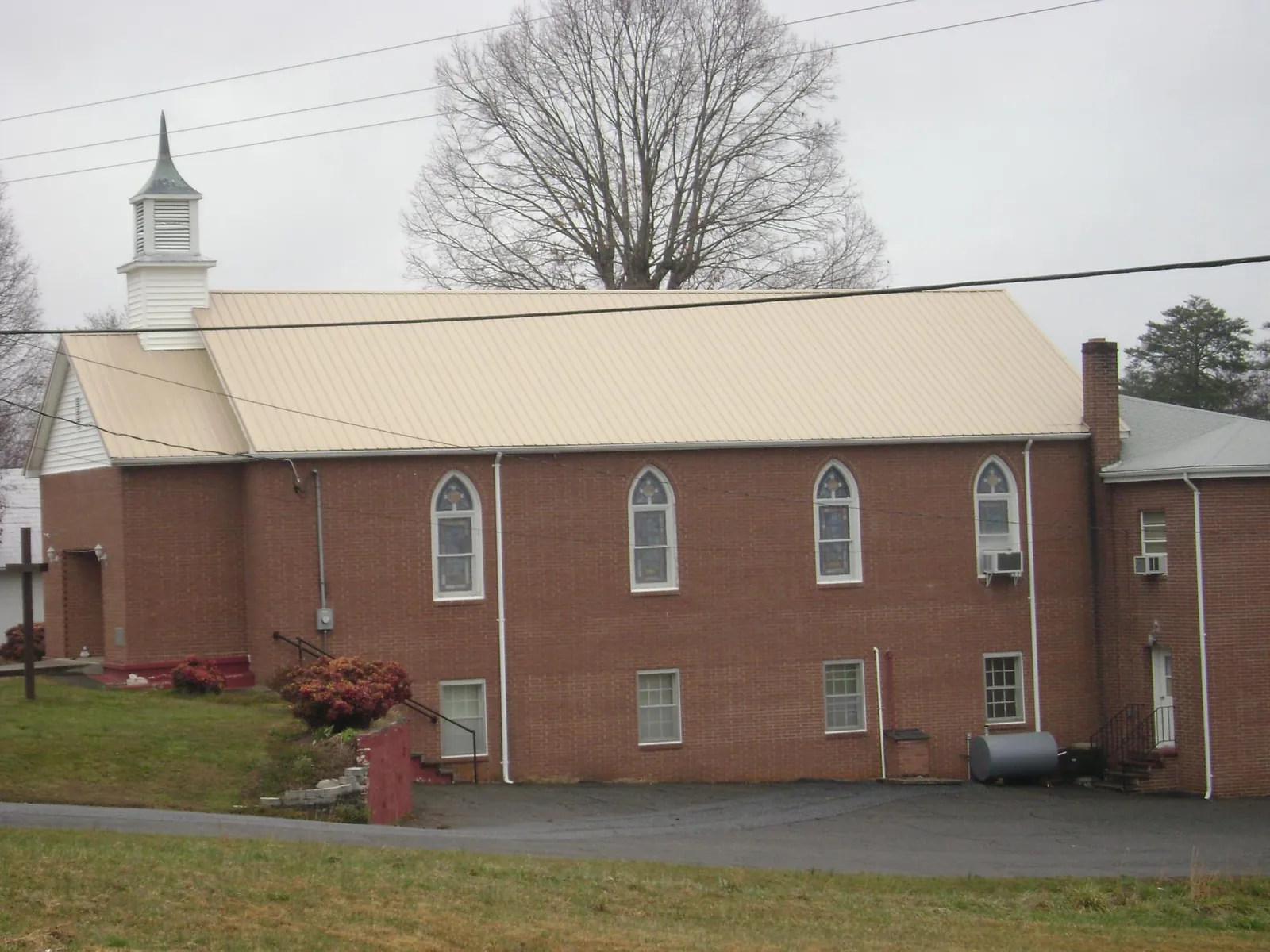 New tan metal roof on a brick church with a white steeple in Haugan