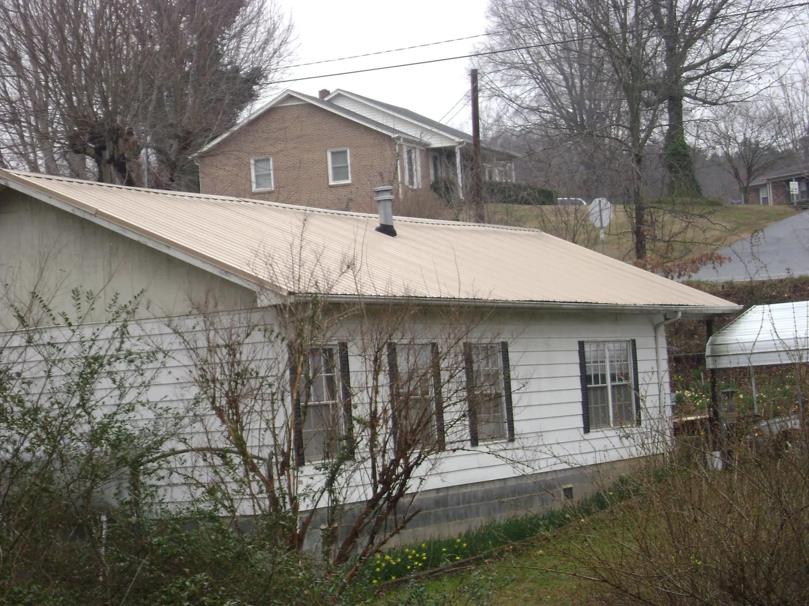 Tan metal roof on a white sided house set into a hillside — Commercial Roofing by Roofing Brothers in Haugan